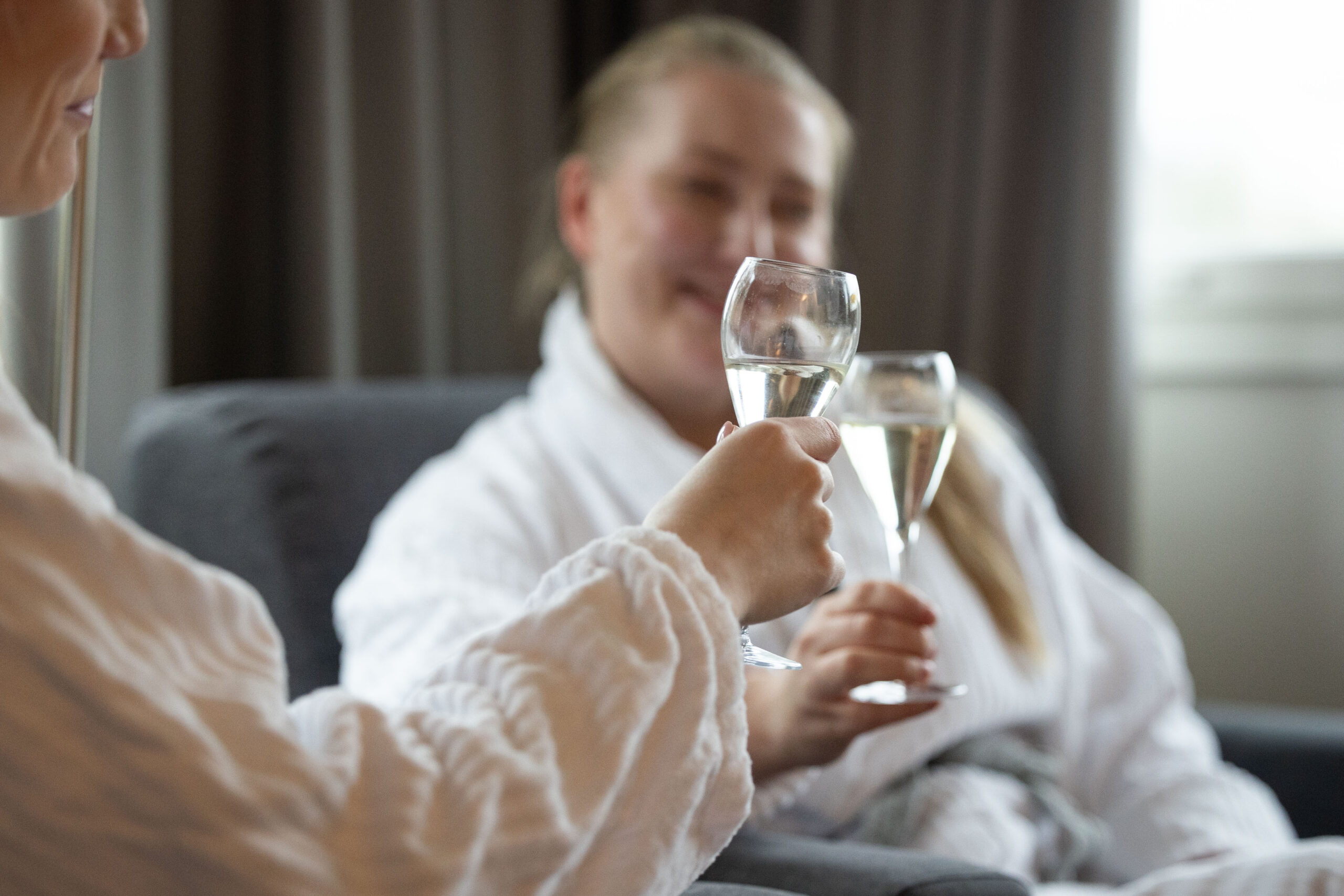 Nainen kohottaa kuohuviinilasin kylpytakissa hotellihuoneessa hääyönä
