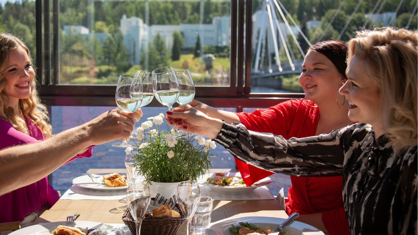 Iloinen seurue kohottaa maljan terassilla järven rantamaisemissa