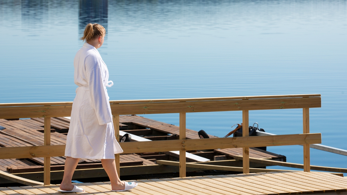 Nainen kylpytakissa kävelee laiturilla järvimaisemissa